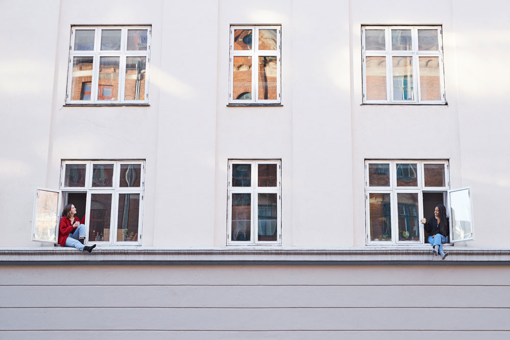 Två tjejer sitter i vars ett fönster i vit byggnad